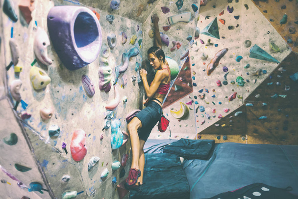 Kraft- und Ausdauertraining. Der Kletterer trainiert an der Kletterwand. Eine Frau trainiert, auf ein künstliches Relief zu klettern. ein schlankes Mädchen treibt Sport. - Foto, Bild