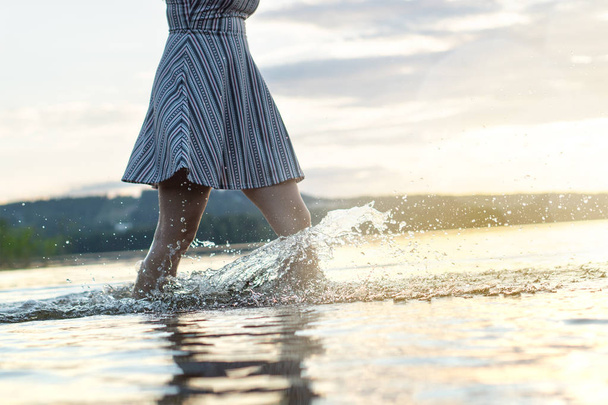 Young attractive woman in sunset. Water splashing when walking in the lake. Carefree and happy summer lifestyle. Hot summer night. - Photo, Image