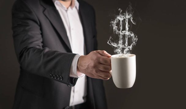 Signo de dólar de vapor de café. Humo formando un símbolo de dinero. Hombre de negocios con traje sosteniendo una bebida caliente en una taza y una taza de té
. - Foto, Imagen