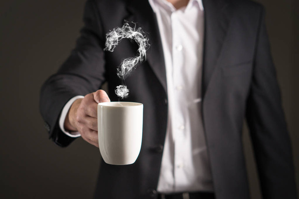 Un signo de interrogación de vapor de café. Humo formando un símbolo. Hombre de negocios con traje sosteniendo una bebida caliente en una taza y una taza de té
. - Foto, Imagen