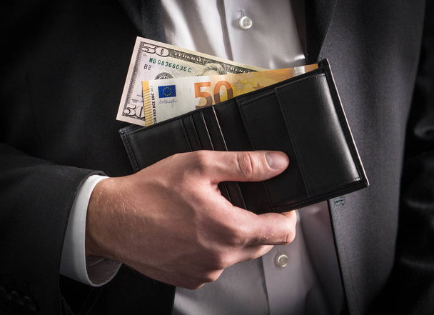 Dollars and euros in wallet. Exchange rate, world economy and financial concept. Business man in a suit with paper money, banknote and bill in hand in both currency. - Fotó, kép