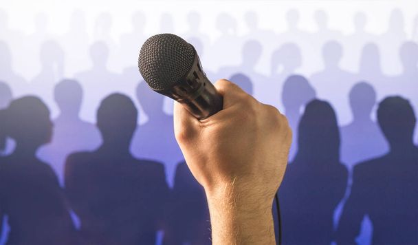 Falar em público e dar conceito de discurso. Mão segurando microfone na frente de um público silhueta e multidão de pessoas. Cantando ao microfone em karaoke ou conceito de show de talentos
. - Foto, Imagem
