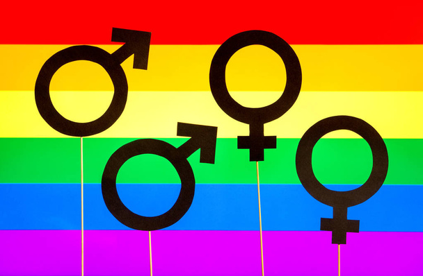 Ομοφυλοφιλία και gay pride πανό. Σύμβολα των δύο φύλων κατά Lgbt σημαία ουράνιο τόξο. Ομοφυλοφιλικό και λεσβιακό ζευγάρι. Έννοια σεξουαλική μειονότητα. Τέσσερα σημάδια χαρτόνι σε ξύλινα ραβδιά και πολύχρωμο φόντο. - Φωτογραφία, εικόνα