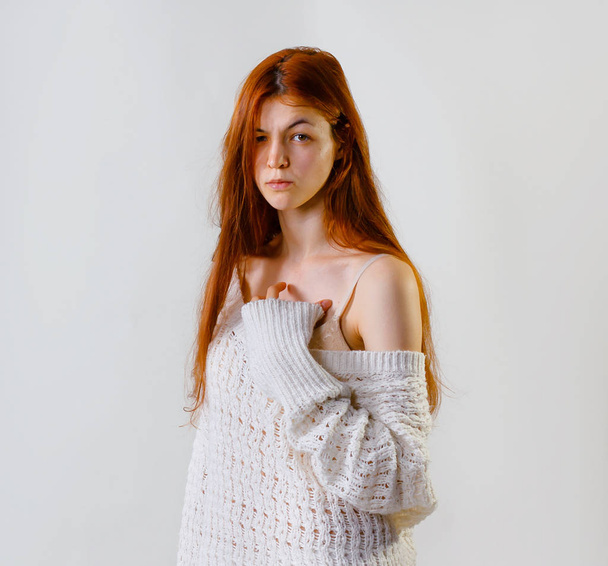 Feeling and emotions. Fashion portrait of cute redhead woman face expression, dressed in knitted sweater looking at camera, naked shoulder while posing on grey background copy space. - Photo, Image