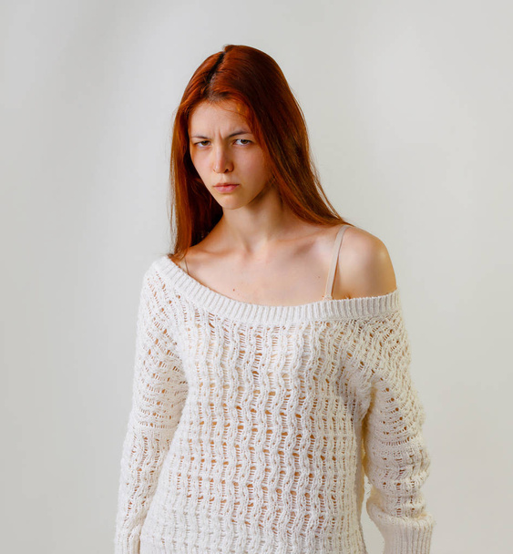 Feeling and emotions. Fashion portrait of cute redhead woman face expression, dressed in knitted sweater looking at camera, naked shoulder while posing on grey background copy space. - 写真・画像