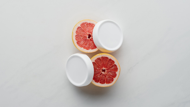 Draufsicht auf Cremeflaschen und Grapefruitstücke auf weißer Oberfläche, Schönheitskonzept - Foto, Bild