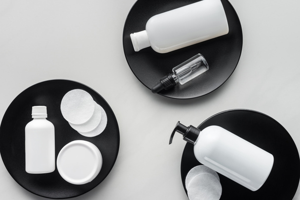 elevated view of bottles of cream and cosmetic pads on three black plates, beauty concept - Zdjęcie, obraz