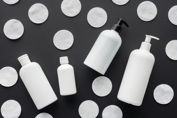 top view of scattered bottles of cream and cosmetic cotton pads isolated on black, beauty concept  - Foto, afbeelding