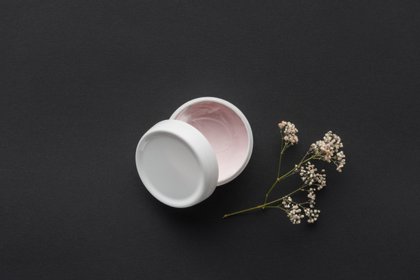 top view of bottle of cream and dried flowers isolated on black, beauty concept - 写真・画像