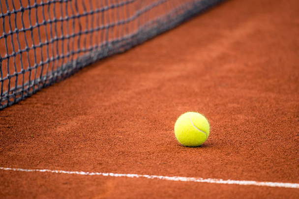 Yellow ball on a clay tennis court next to the net. - Zdjęcie, obraz
