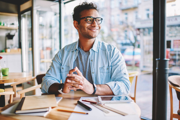 Handsome smiling smart male entrepreneur enjoying work break and pondering about creative ideas for business startup.Mature clever positive man in stylish eyeglasses looking away while sitting in cafe - Foto, Bild