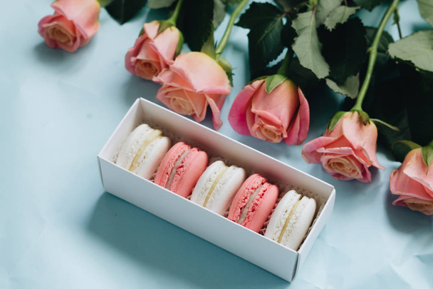 composition of delicious macaroons and pink roses on blue table - Φωτογραφία, εικόνα