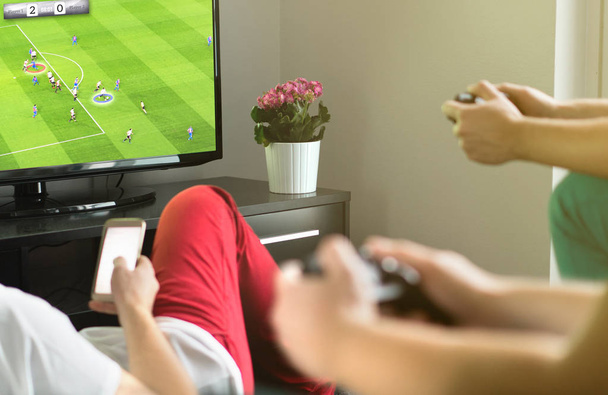 Group of friends hanging out and playing imaginary soccer or football video game with console and tv. Guys night, party and weekend concept. - Photo, image