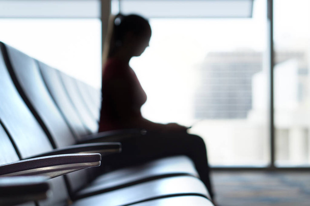 Siluetti nainen lentokentän odotushuoneessa. Henkilö istuu penkillä ennen lentoa terminaalissa ja lähtöaulassa. Matkailu, loma ja kuljetus käsite
. - Valokuva, kuva
