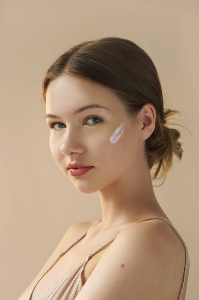 retrato de jovem com creme cosmético no rosto em fundo bege
  - Foto, Imagem