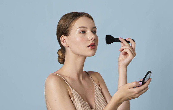 retrato de mujer joven aplicando polvo cosmético en su cara sobre fondo azul
  - Foto, Imagen
