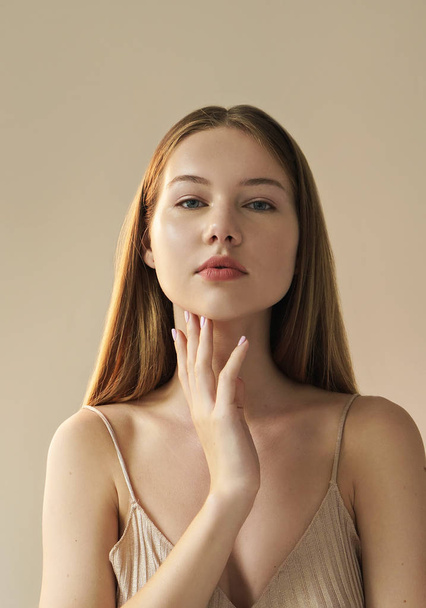 portrait of young woman touching her chin posing on beige background  - Photo, Image