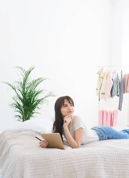 молода щаслива жінка купує онлайн за допомогою цифрового планшета, лежачого в ліжку вдома
  - Фото, зображення