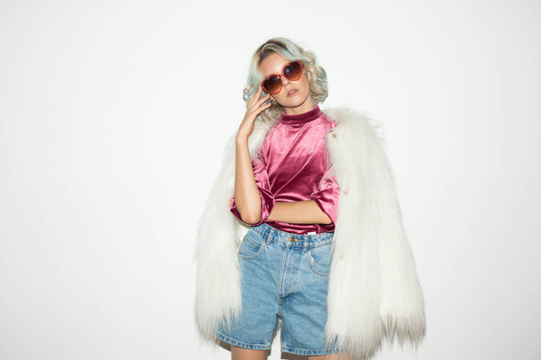 Beautiful fashion girl in white fur jacket and sunglasses dreamily looking in camera over white background  - Fotografie, Obrázek