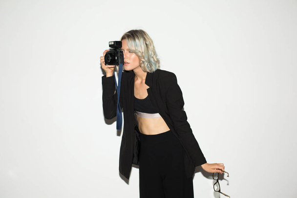Fiatal hölgy elgondolkodva fotózni a retro fényképezőgép szemüveg a kéz felett fehér háttér, fekete klasszikus ruha  - Fotó, kép