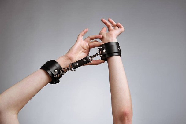 hands of woman in leather handcuffs against studio background  - Foto, Imagem