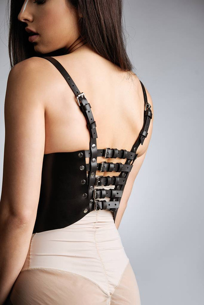 Sensual young woman in harness belts posing against studio background       - Foto, afbeelding