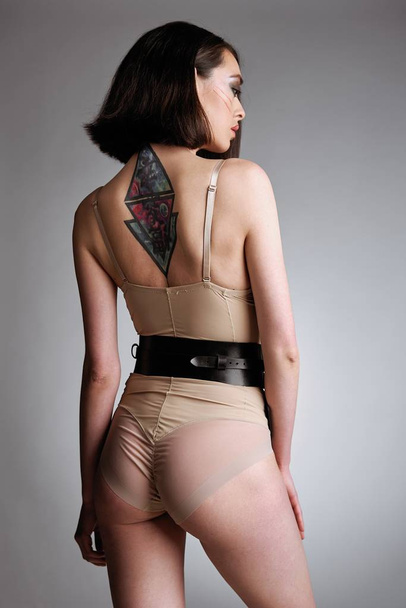 Sensual young woman in harness belts posing against studio background                        - Φωτογραφία, εικόνα