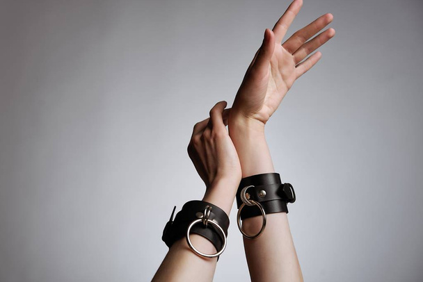 hands of woman in leather handcuffs against studio background  - Fotó, kép