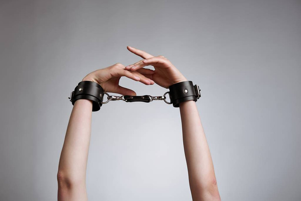 hands of woman in leather handcuffs against studio background  - Photo, image