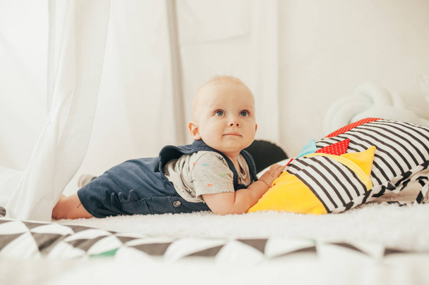 Toddler in rompers and t-shirt lies on bed next to colorful pillows. - Photo, Image