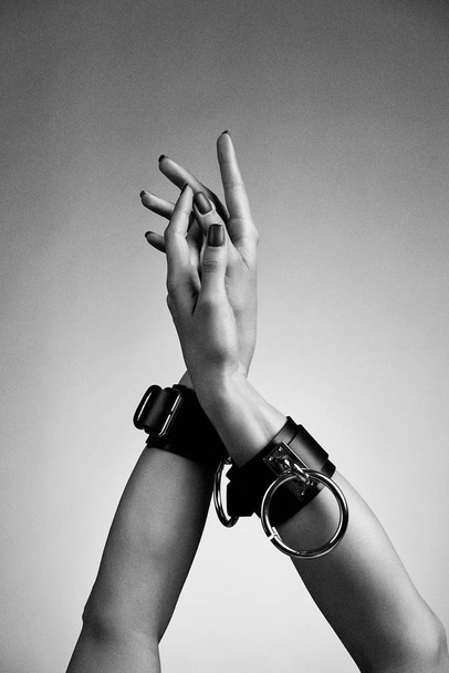 hands of woman in leather handcuffs against studio background  - 写真・画像