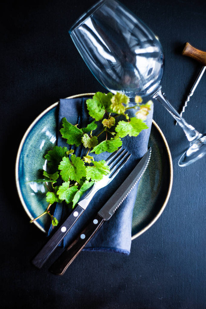 Rustic table setting decorated with green leaves of grape vine on dark wooden table with copy space - Foto, Imagem