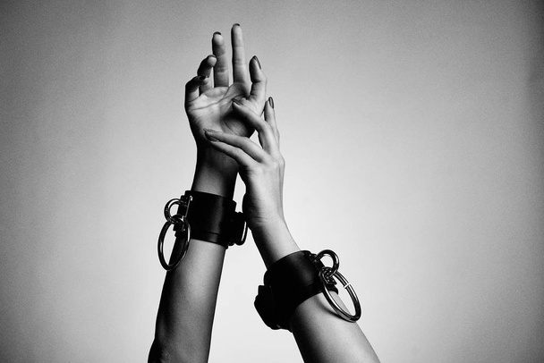 hands of woman in leather handcuffs against studio background  - Фото, изображение