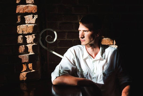 Retrato de un hombre con una camisa blanca, mirando a un lado, pared de ladrillo en su fondo y sol cálido brillando en su cara
 - Foto, Imagen