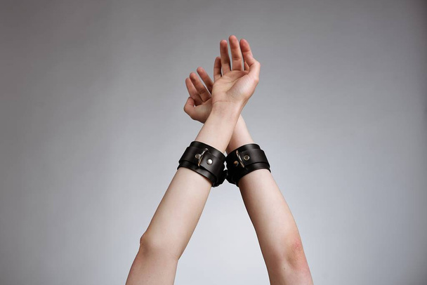 hands of woman in leather handcuffs against studio background  - Foto, Imagem