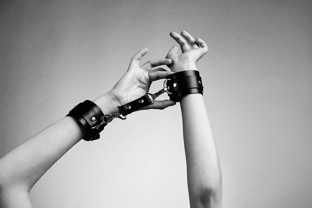 hands of woman in leather handcuffs against studio background  - Valokuva, kuva