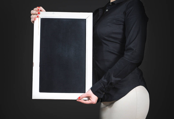 Waitress holding empty chalkboard. Young professional woman in black shirt with blank blackboard. Negative copy space for restaurant menu, cafe specials or happy hour deals in a bar. Dark background. - 写真・画像