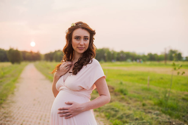 Retrato de una mujer embarazada feliz en un parque al amanecer con una cálida luz de fondo rosa
. - Foto, Imagen