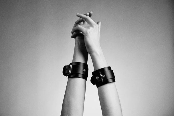 hands of woman in leather handcuffs against studio background  - Photo, Image