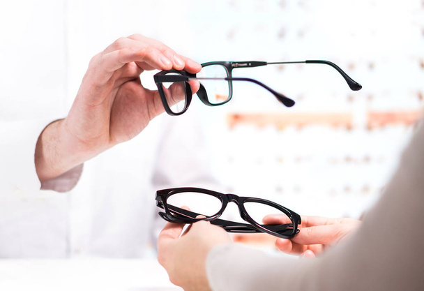 Мбаппе подарил новые очки клиенту для тестирования и испытаний. Глазной врач показывает линзы пациентов в магазине очков. Профессиональный оптик в белом халате с клиентом
. - Фото, изображение
