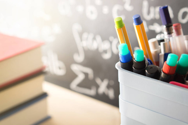 Pen holder and books in front of blackboard in classroom. Education, learning, teaching and knowledge concept. Classroom with chalkboard and school stuff. Happy and sunny summer vibe. - Фото, зображення