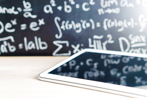 Modern education and e learning concept. Tablet in front of a blackboard full of writing at school. Smart mobile device and chalkboard in classroom. Learning with technology. Digital exam. - Foto, Imagem