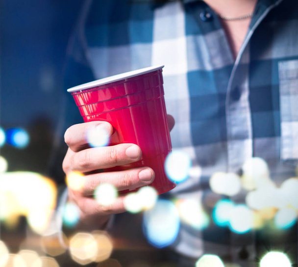 Joven sosteniendo una taza roja en una fiesta de lujo. Persona que se divierte y bebe alcohol. Concepto de celebración abstracto y moderno
. - Foto, imagen