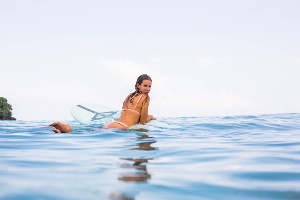 Beautiful surfer lady in sexy pink bikini rest in ocean water on surfing longboard. Girl have fun during hot summer day at tropic island resort, relax vacation concept. Hipster lifestyle advertising. - 写真・画像