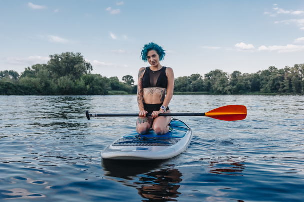 bela tatuado menina esportiva sentado no paddle board no rio
 - Foto, Imagem