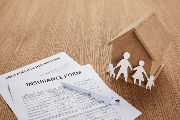 close-up view of insurance form, insurance health claim form, pen, small house and paper cut family on wooden table - Photo, Image