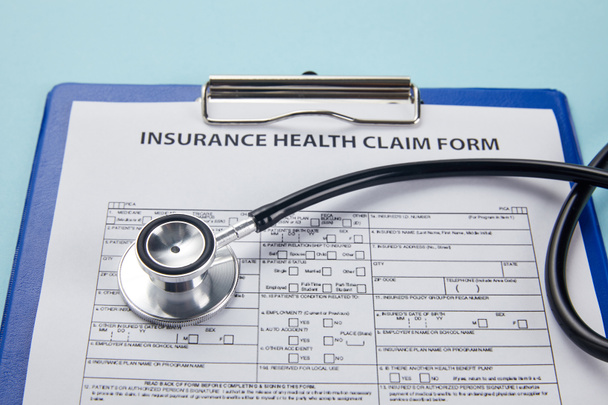 close-up view of insurance health claim form on clipboard and stethoscope on blue   - Photo, Image