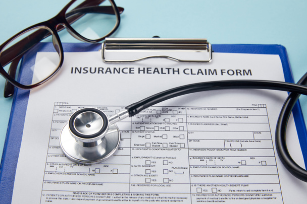 Nahaufnahme von Versicherungsformular, Klemmbrett, Brille und Stethoskop auf blau   - Foto, Bild