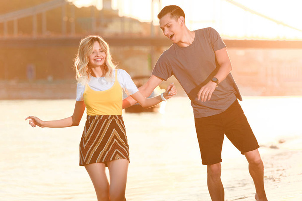 laughing young couple having fun on river beach during sunset - Foto, imagen
