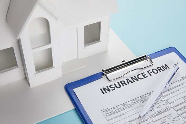 Close-up weergave van verzekeringsformulier en klein huis model met Klembord en pen in blauw  - Foto, afbeelding
